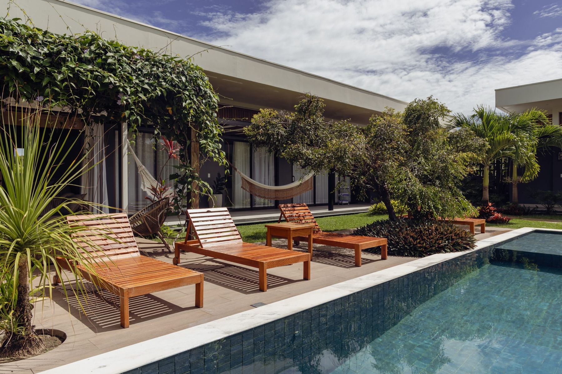 Casa térrea com piscina, espreguiçadeiras e jardim tropical